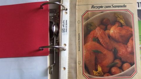 Ein Rezeptbuch steht offen und zeigt ein Gericht mit Kürbis und Kastanien, umgeben von einem roten Ordner.