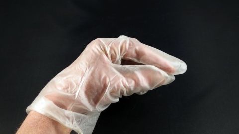 Eine Hand mit einem Einweg-Handschuh hält vorsichtig Shampoo, um die Hände beim Haarewaschen zu schonen.