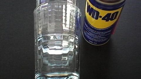 Ein WD-40 Spray steht neben einem leeren Glas auf einem schwarzen Tisch, bereit für vielfältige Anwendungen im Haushalt.
