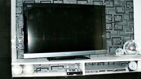 Ein schwarzer Fernseher hängt an der Wand, kabelgeschützt, vor einem stilvollen, geometrischen Hintergrund.