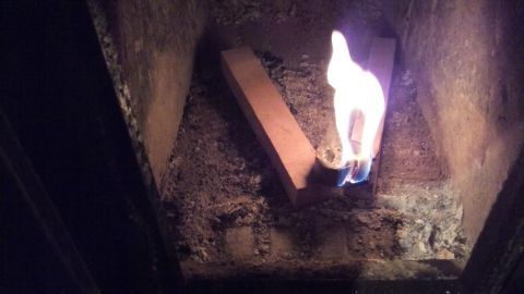 Flammende Kaminanzünder brennen in einem Kamin, während Holzstücke im Hintergrund liegen und eine hohe Rauchentwicklung erzeugen.