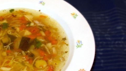 Eine Schüssel asiatische Hühnersuppe dampft appetitlich auf einem weißen Teller, umgeben von einem blauen Hintergrund.