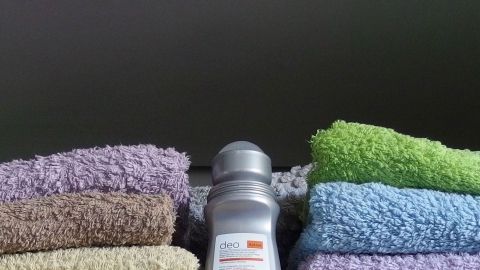 Auf einem Regal sind farbige Handtücher angeordnet, während ein Deo als Schrankerfrischer in der Mitte platziert ist.