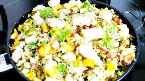 Eine bunte Pfanne mit Kabeljau, Bulgur, Zucchini und Paprika wird auf einem Herd in einer modernen Küche zubereitet.