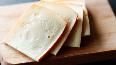 Mit diesem einfachen Trick kann man Käse und harte Butter viel einfacher schneiden. Auf einem Holzbrett liegt frisch geschnittener Käse, der ordentlich in Scheiben angeordnet ist.