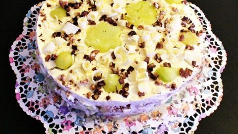 Eine Mascarpone-Melonentorte auf einem Reiswaffelboden, dekoriert mit Melonenscheiben und Schokoladenstückchen, steht auf einem filigranen Teller.