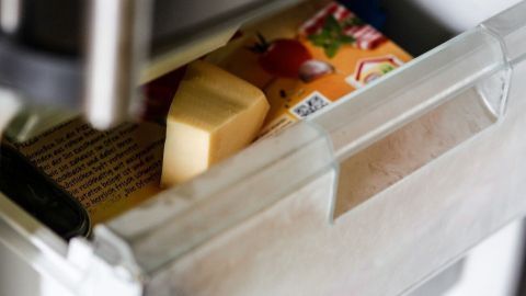 In einem Kühlschrankaufsatz liegt ein Stück Käse, bereit zum Reiben, während ein Riegel neben ihm auf einer Schublade liegt.