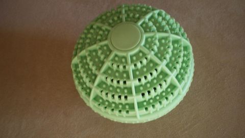 Ein grüner Öko-Waschball liegt still auf einer beige Oberfläche. Sein Design ist strukturiert und rund.