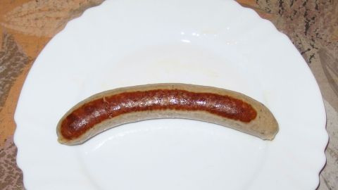 Auf einem weißen Teller liegt eine Thüringer Wurst, glänzend und appetitlich, bereit zum Genießen in einer gemütlichen Küche.