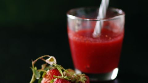 Ein Glas alkoholfreie Altbierbowle mit frischen Erdbeeren wird gefüllt, während die Pflanzen im Hintergrund leicht verschwommen sind.