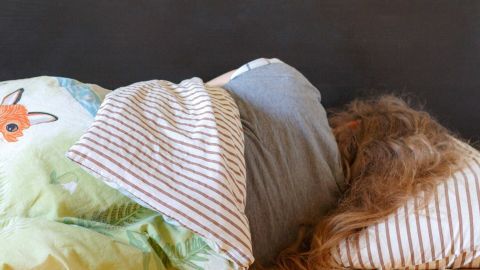 Eine Person liegt schlafend auf der linken Seite, eingekuschelt in Decken, in einem gemütlichen Schlafzimmer.