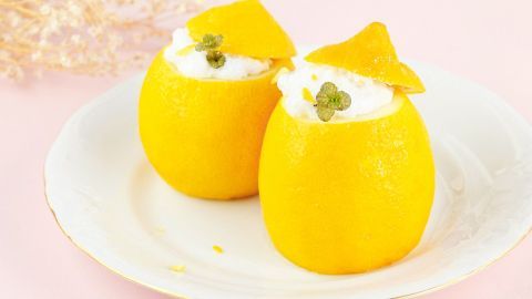 Zwei halbe Zitronen, gefüllt mit Zitronensorbet und Sahne, stehen auf einem weißen Teller vor einem rosa Hintergrund.