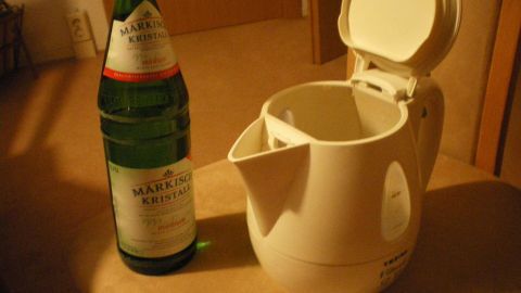Ein Wasserkocher steht offen auf einem Tisch neben einer Flasche Sprudelwasser, bereit, Kalk im Wasserkocher zu reduzieren.
