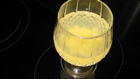 Ein Glas mit gelber "Kalte Ente" Bowle steht auf einem dunklen Induktionskochfeld, bereit zum Servieren. Kein Text vorhanden.