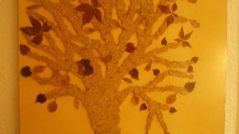 Ein Baum ist aus bunten Blättern gestaltet, umgeben von weiteren Blättern auf einem hellen Hintergrund.