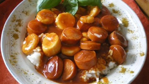 Auf einem Teller liegen geschnittene Currywürste und Banane, angerichtet in einer reichhaltigen, würzigen Soße.