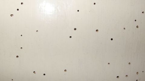 Kleine Löcher sind auf einer hellen Holzoberfläche verteilt, was auf den Befall von Holzwürmern hinweist.