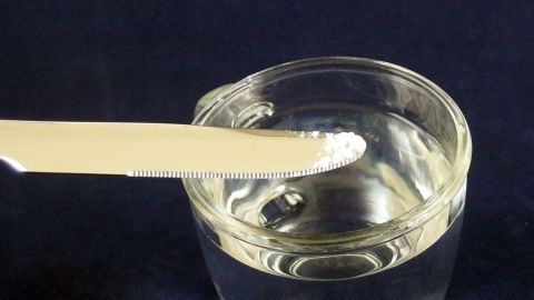 Ein Löffel mit Backpulver steht über einem Glas Wasser, während es darauf wartet, in die Flüssigkeit gegeben zu werden.