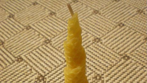 Eine gelbe, spiralförmige Kerze steht auf einem braunen Tonteller in einem gemütlichen Raum mit einem gemusterten Teppich.
