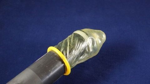 Ein Kondom sitzt an einem Staubsaugerrohr, um Spinnen beim Einsaugen sicher zu halten. Der Hintergrund ist einellblau.