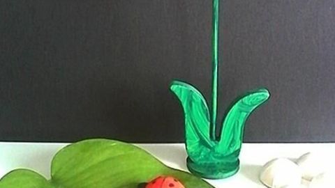 Rote Marienkäfer aus Gips stehen auf einem grünen Blatt, umgeben von einer Tulpe als Dekoration im Hintergrund.