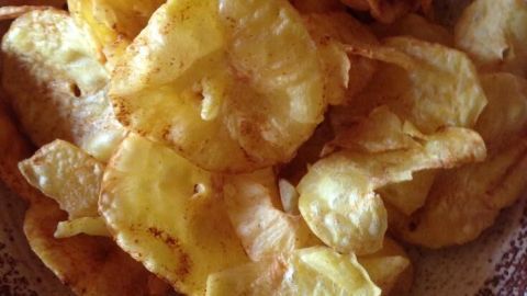 Auf einem Teller liegen goldene Diät-Kartoffel-Chips, knusprig und appetitlich, bereit zum Verzehr.