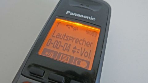 Kämpfe gegen aufdringliche Call Center Agents mit einem simplen Trick: Schrecke sie mit unorthodoxen Antworten ab. Dein Telefon wird zum Verbündeten im Kampf gegen unerwünschte Anrufe. Telefon mit orangefarbenem Display zeigt "Panasonic, Lautsprecher, 0-00-04, Vol." in Nahaufnahme auf hellem Hintergrund.