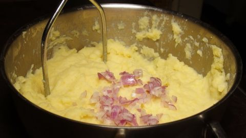 Einfache, cremige Kartoffelpüree mit Zwiebeln wird in einem Topf mit einem Kartoffelstampfer zubereitet.