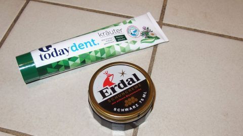 Schuhcreme an eine falsche Stelle bekommen? Mit Zahncreme bekommt man den Fleck wieder weg. Eine Tube Zahnpasta liegt neben einer Dose Schuhcreme auf einem hellen Fliesenboden, bereit zum Reinigen.