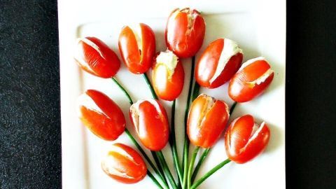 Ein Strauß aus präparierten Tomaten sieht aus wie frische Tulpen, arrangiert auf einem weißen Teller vor schwarzem Hintergrund.