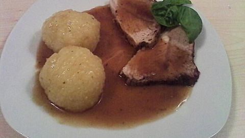 Zartes Schweinebratenstück liegt auf einem Teller, umgeben von zwei Kartoffelknödeln in reichhaltiger Sauce.