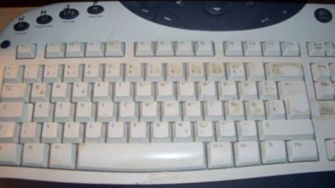 Die Computer-Tastatur, leicht verschmutzt und verstaubt, liegt auf einem dunklen Tisch, ohne sichtbare Klarsichtfolie.