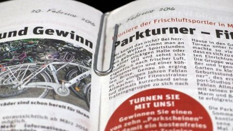Eine aufgeschlagene Zeitung zeigt einen Artikel über Parkturner und beinhaltet Werbung, die zur aktiven Teilnahme aufruft.