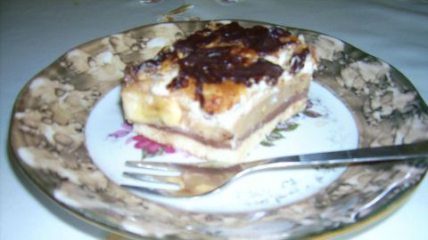 Ein Stück Schoko-Karamell-Bananenkuchen liegt auf einem blumengemusterten Teller mit einer Gabel daneben, umgeben von hellem Tisch.
