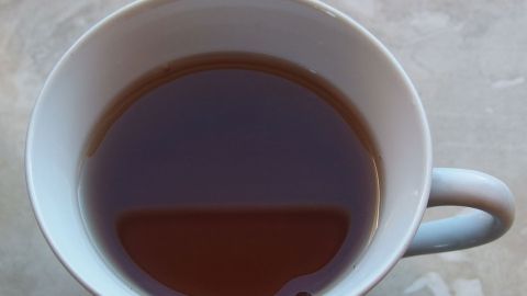 Eine Tasse Tee steht auf einer glatten Oberfläche, gefüllt mit warmem, dunklem Tee, bereit zum Genießen.