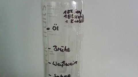 Ein Glas Dressing-Mixer mit einer Skala enthält öl und Zutaten wie Balsamico und Sahne, geschrieben auf der Seite.