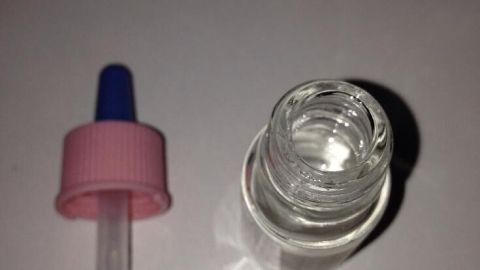 Eine Glasflasche mit Duftöl steht auf einem weißen Tisch, daneben liegt eine Pipette zum genauen Dosieren.