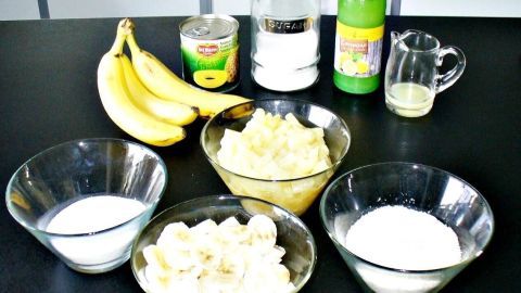 Bananenstücke und Kokosmilch liegen in Schalen, umgeben von Ananas und Zutaten für einen exotischen Aufstrich.