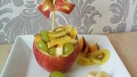 Ein auf einem Teller arrangierter Apfel mit bunten Früchten gefüllt, präsentiert auf einem dekorativen Hintergrund.