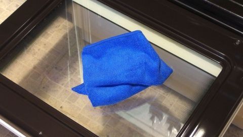 Eine blaue Reinigungstuch liegt auf einer sauberen Glas-Ofentür, während sie zum Reinigen vorbereitet wird.
