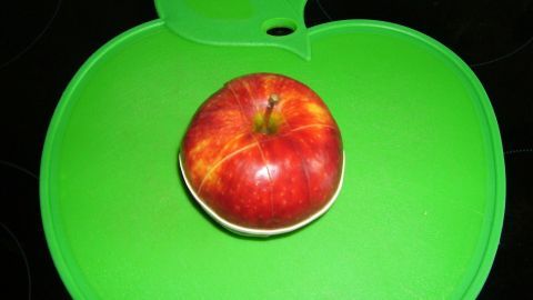 Ein roter, geschnittener Apfel liegt auf einem grünen, apfelförmigen Schneidebrett in einer modernen Küche.