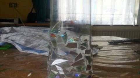 Eine alte Vase mit bunten Mosaikstücken steht auf einem Tisch in einem hellen Raum und reflektiert das Licht.
