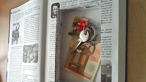 Ein Buch zeigt einen ausgehöhlten Innenraum, der Schlüssel und Geld als DIY-Buchsafe versteckt; liegt auf einem Holztisch.