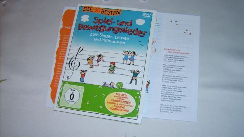 Ein bunter DVD-Cover für Kindergartenkinder mit fröhlichen Figuren, um das Spielen und Singen zu fördern, liegt auf einem Tisch.