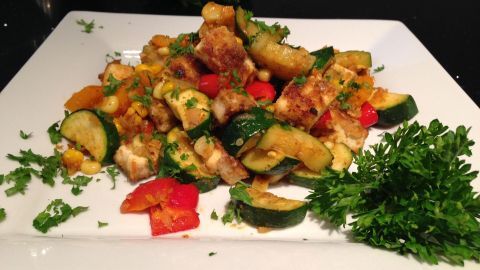 Knusprig gebratener Tofu liegt neben buntem Gemüse wie Zucchini und Paprika auf einem weißen Teller, garniert mit frischer Petersilie.