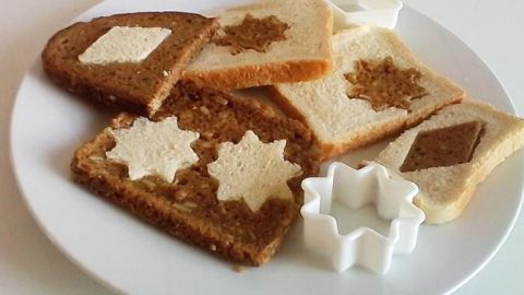 Mix verschiedene Brotscheiben kreativ und richte sie an, wie in diesem Beispiel. Die Kombination aus hellem und dunklem Brot sorgt nicht nur für Abwechslung, sondern macht dein Brotessen auch optisch zu einem Highlight. Bunte Brotscheiben liegen auf einem Teller, dekorativ angeordnet mit verschiedenen, essbaren Mustern und Formen.