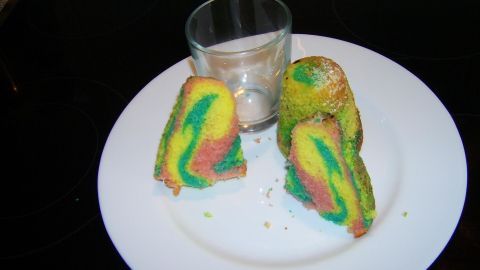Bunte, marmorierte Kuchenstücke liegen auf einem weißen Teller, während ein leeres Glas für Duftkerzen daneben steht.