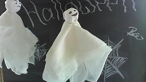 Zwei fliegende Halloween-Gespenster hängen über einer Tafel, auf der "Halloween" geschrieben steht, umgeben von Spinnennetzen.