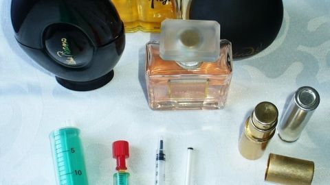 Schwarze und transparente Parfumpullen liegen um eine Spritze und andere Utensilien, um Parfum leicht umzufüllen.