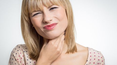 Eine Frau fasst sich mit einer Hand an den Hals und zeigt ein schmerzhaftes Gesicht, während sie an Rachenbeschwerden leidet.